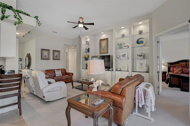 living room featuring built in shelves, light colored carpet, and ceiling fan