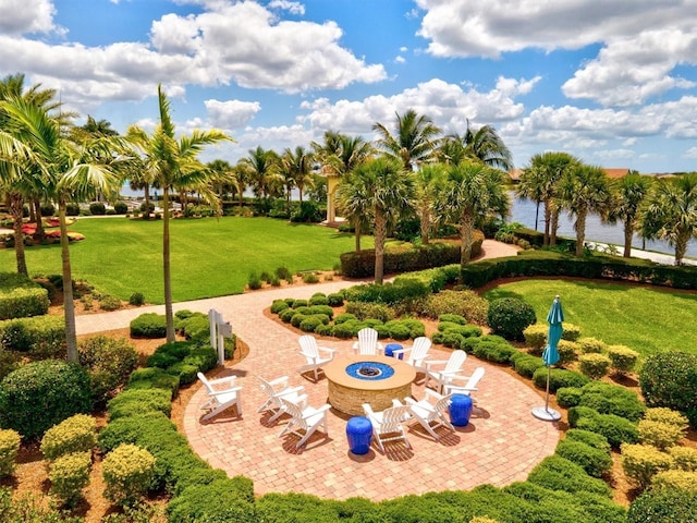 view of home's community with a fire pit, a water view, a patio, and a lawn