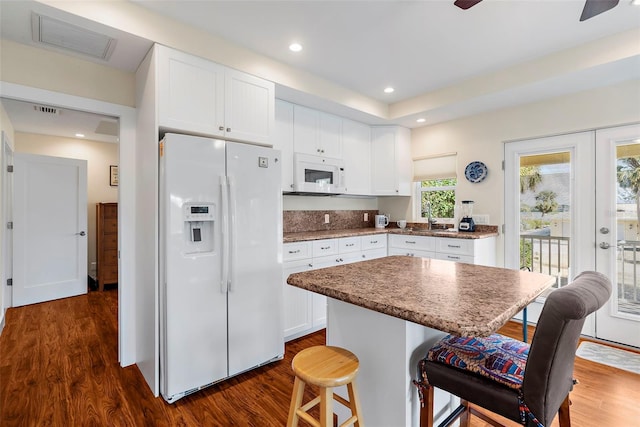 kitchen featuring a center island, dark hardwood / wood-style floors, white appliances, a breakfast bar area, and white cabinets