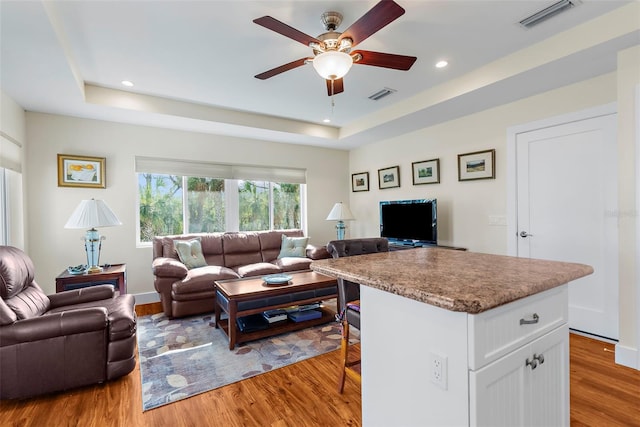 living room featuring hardwood / wood-style flooring, ceiling fan, and a tray ceiling