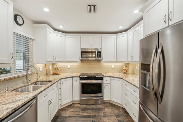 kitchen with decorative backsplash, light stone countertops, stainless steel appliances, sink, and white cabinetry