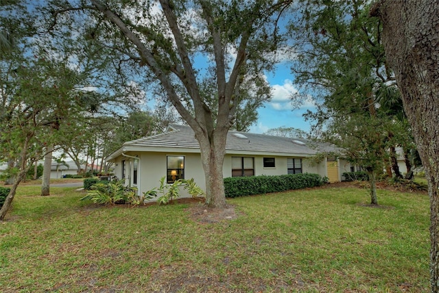 view of front facade with a front yard, a tile roof, and stucco siding