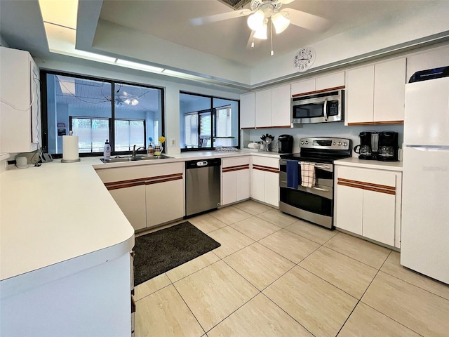 kitchen with appliances with stainless steel finishes, a tray ceiling, light countertops, and a sink