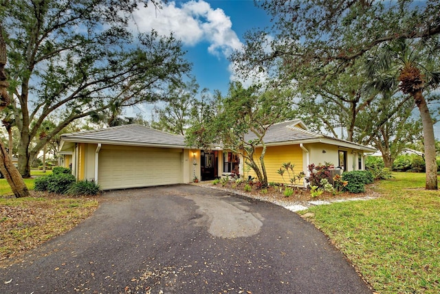 ranch-style home with a front yard, a tile roof, driveway, and an attached garage