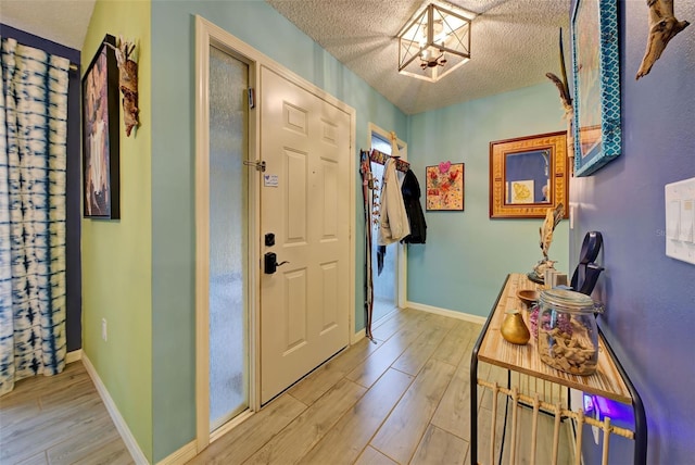 foyer entrance featuring light wood finished floors, baseboards, and a textured ceiling