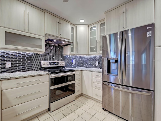 kitchen with light stone countertops, stainless steel appliances, under cabinet range hood, backsplash, and light tile patterned flooring
