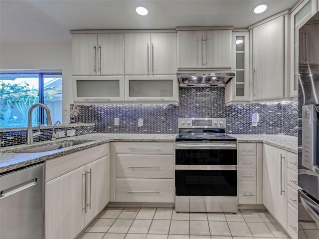 kitchen featuring stainless steel appliances, light tile patterned flooring, wall chimney range hood, and a sink