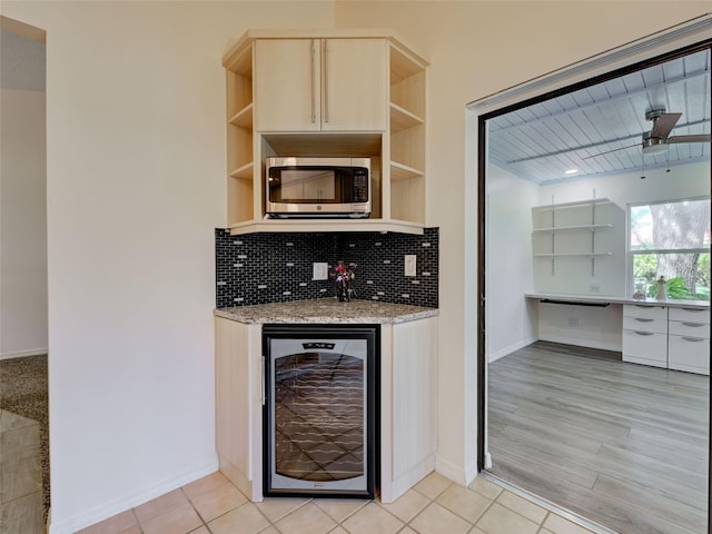 bar with stainless steel microwave, tasteful backsplash, bar, baseboards, and beverage cooler