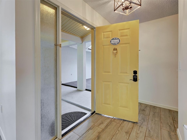 foyer featuring a textured ceiling, baseboards, a chandelier, and light wood-style floors
