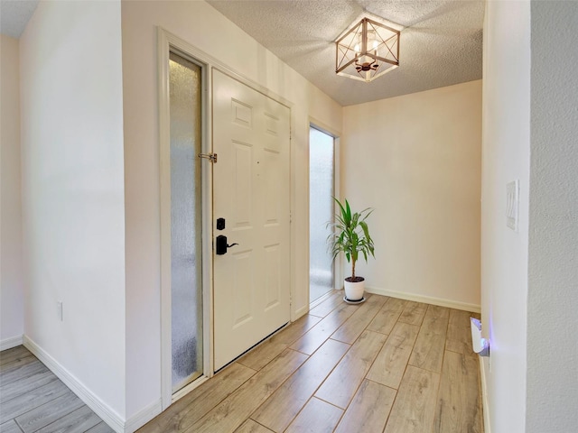 foyer featuring a chandelier, baseboards, a textured ceiling, and light wood-style flooring