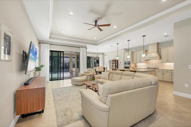 tiled living room with ceiling fan and a tray ceiling