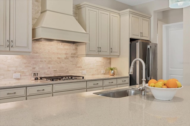 kitchen with sink, light stone countertops, appliances with stainless steel finishes, tasteful backsplash, and custom range hood