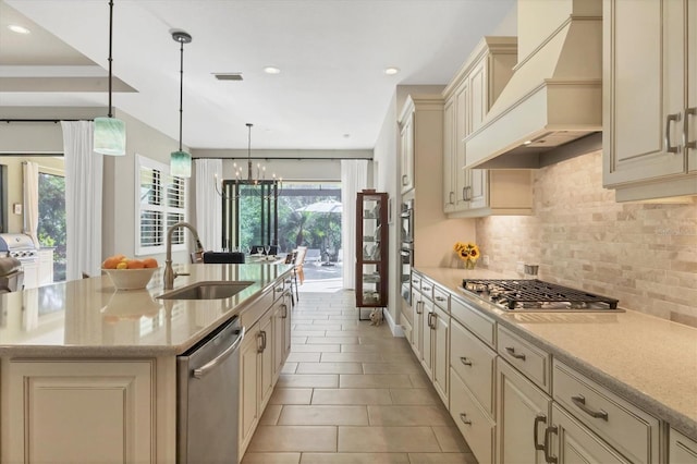 kitchen featuring sink, premium range hood, decorative light fixtures, a kitchen island with sink, and appliances with stainless steel finishes