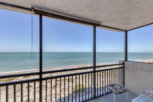 unfurnished sunroom featuring a view of the beach and a water view