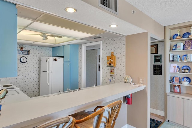 kitchen featuring kitchen peninsula, a kitchen bar, blue cabinets, sink, and white refrigerator