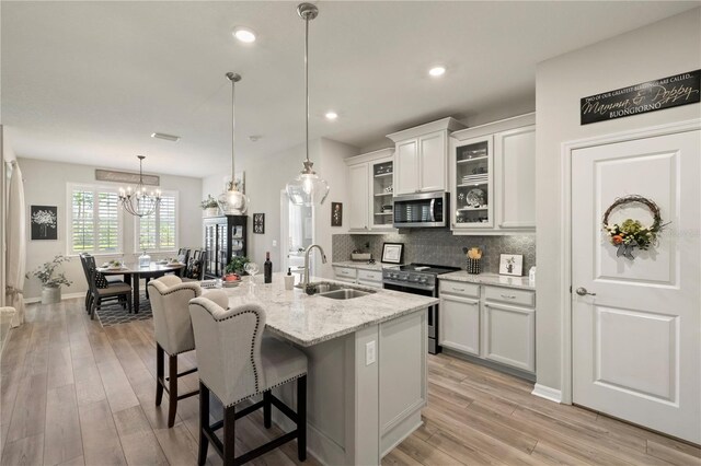 kitchen with a center island with sink, white cabinets, glass insert cabinets, light stone countertops, and stainless steel appliances