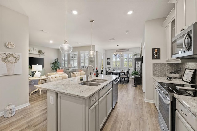 kitchen featuring stainless steel appliances, hanging light fixtures, open floor plan, a sink, and an island with sink