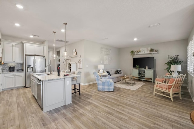 kitchen featuring pendant lighting, sink, white cabinets, stainless steel appliances, and a center island with sink