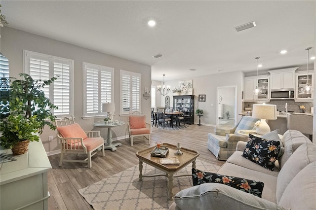 living area with recessed lighting, visible vents, light wood-style flooring, an inviting chandelier, and baseboards