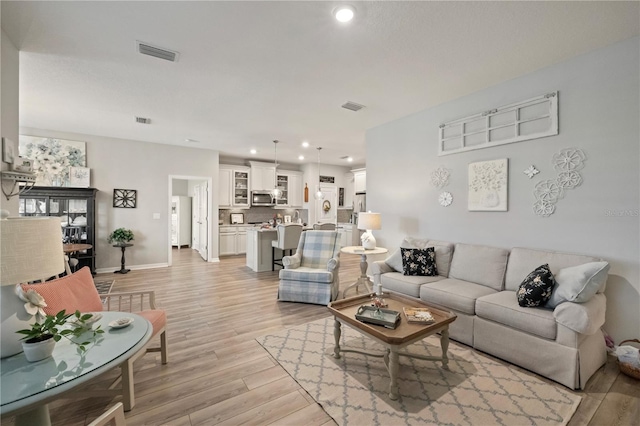 living area with light wood-type flooring, visible vents, baseboards, and recessed lighting