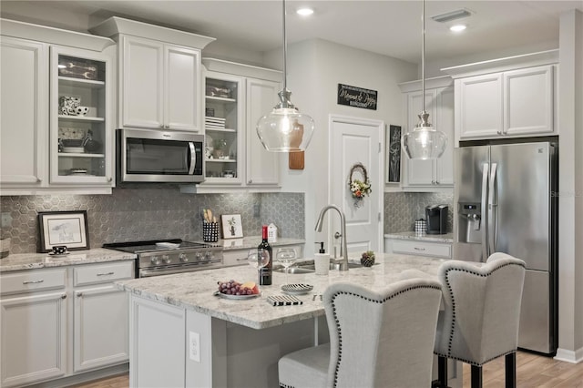 kitchen with glass insert cabinets, stainless steel appliances, a sink, and decorative light fixtures