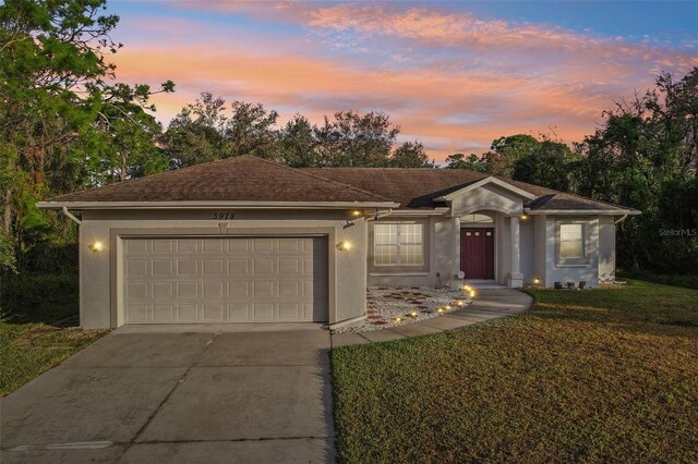 ranch-style house featuring a garage, a yard, driveway, and stucco siding