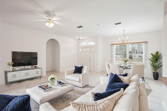 living area with ceiling fan with notable chandelier, arched walkways, visible vents, and light tile patterned floors