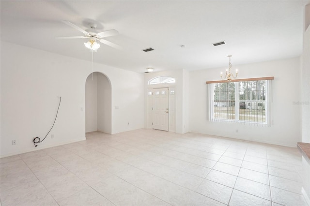 empty room featuring light tile patterned floors, visible vents, arched walkways, and ceiling fan with notable chandelier