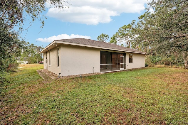 rear view of house featuring a sunroom, a lawn, and stucco siding