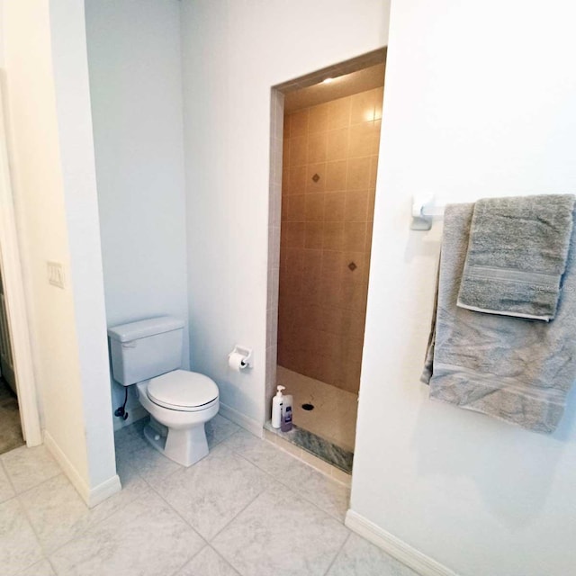 full bath featuring baseboards, tiled shower, toilet, and tile patterned floors