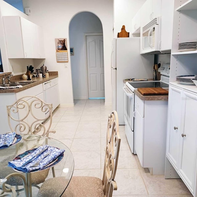 kitchen featuring arched walkways, white cabinetry, a sink, light tile patterned flooring, and white appliances