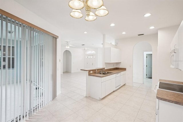 kitchen with a peninsula, white cabinetry, arched walkways, and a sink