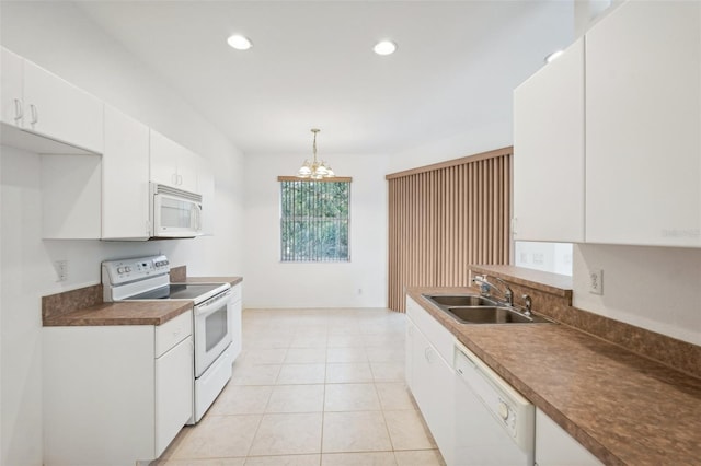 kitchen featuring white appliances, a sink, white cabinets, hanging light fixtures, and dark countertops