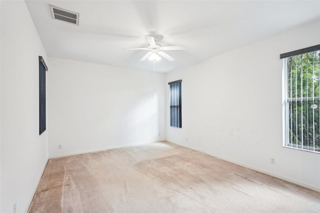 spare room with a ceiling fan, visible vents, light carpet, and baseboards