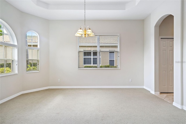 unfurnished room with a raised ceiling, a notable chandelier, light colored carpet, and plenty of natural light