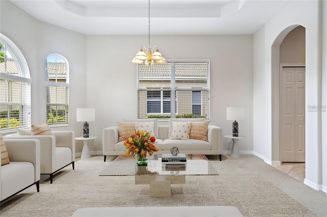 unfurnished living room featuring a raised ceiling, light carpet, and an inviting chandelier