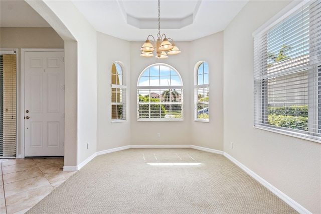 carpeted empty room with a raised ceiling and a notable chandelier