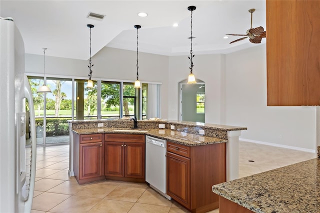 134 Savona Way N, Venice, FL 34275 - kitchen with white dishwasher, freestanding refrigerator, brown cabinetry, a ceiling fan, and light stone counters