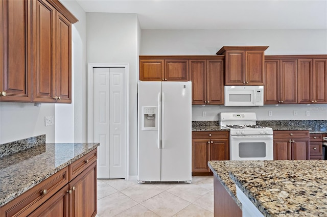 kitchen with dark stone countertops, light tile patterned floors, and white appliances