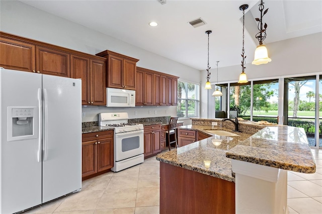 kitchen featuring sink, dark stone countertops, decorative light fixtures, white appliances, and a kitchen island with sink