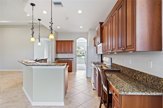 kitchen featuring decorative light fixtures, a center island, dark stone countertops, and white gas range oven