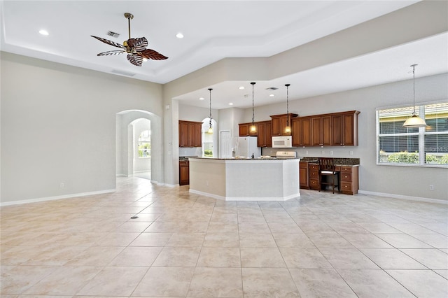 kitchen featuring a center island with sink, white appliances, hanging light fixtures, and a wealth of natural light