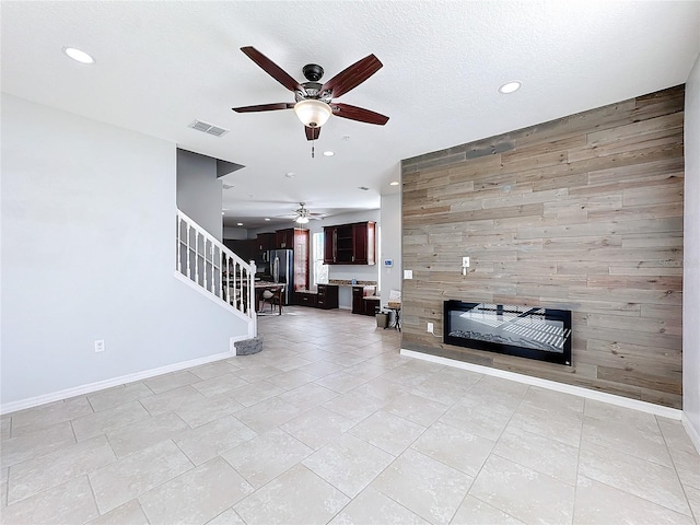 unfurnished living room featuring ceiling fan, a fireplace, a textured ceiling, and wooden walls