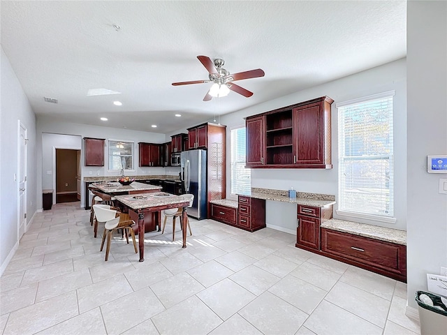 kitchen with appliances with stainless steel finishes, light stone counters, ceiling fan, and a healthy amount of sunlight