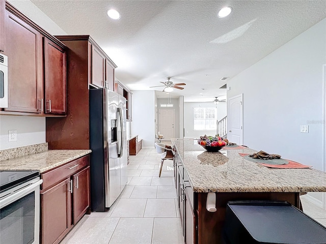 kitchen with a center island, ceiling fan, a textured ceiling, light stone counters, and stainless steel appliances