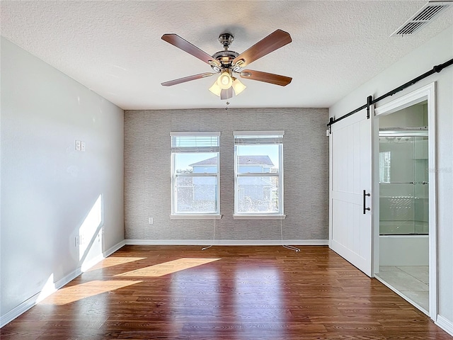 empty room featuring wood-type flooring, a barn door, a textured ceiling, and ceiling fan