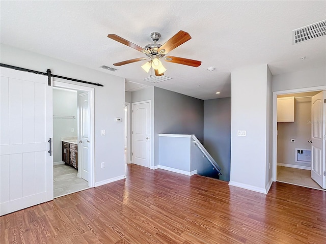 empty room featuring a barn door, ceiling fan, a textured ceiling, and light wood-type flooring