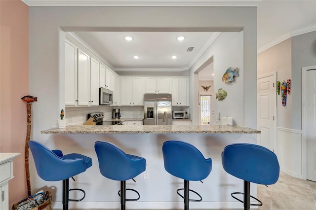 kitchen with light stone countertops, a kitchen bar, white cabinetry, stainless steel appliances, and backsplash