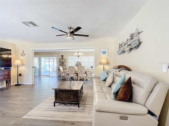 living room featuring hardwood / wood-style flooring, ceiling fan with notable chandelier, and a textured ceiling