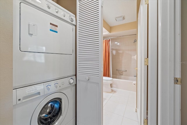 washroom with stacked washer / drying machine, light tile patterned floors, and a textured ceiling